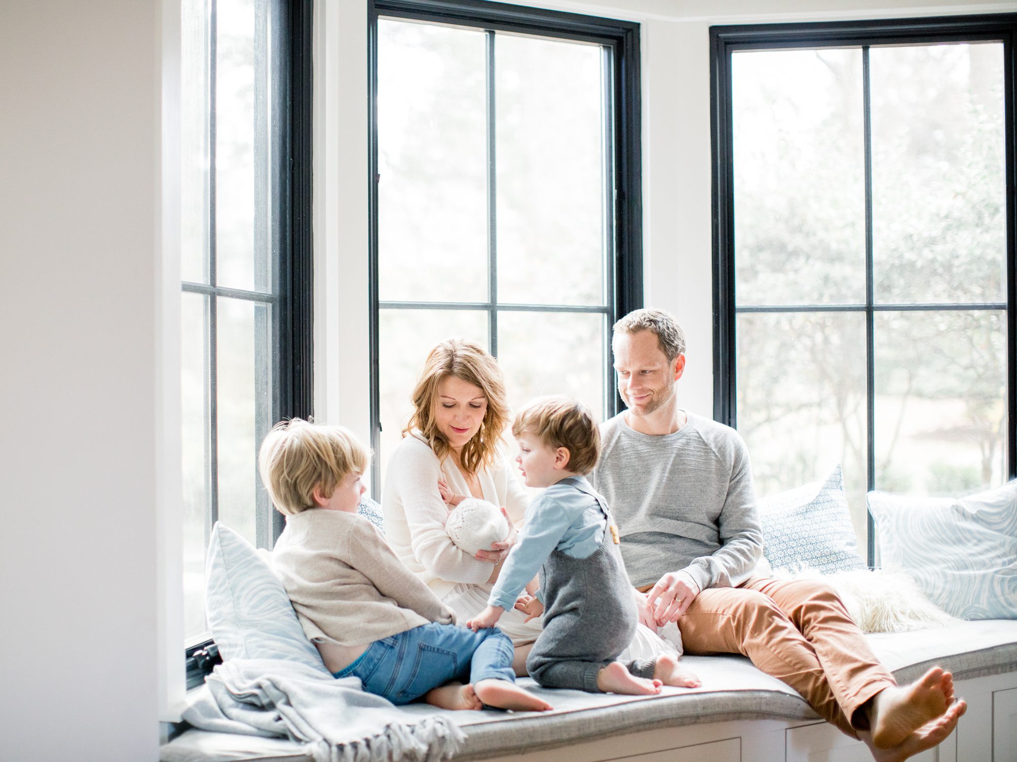 Family with new baby sitting on window seat during session. Photo by Chevy Chase DC Newborn photographer, LRG Portraits.