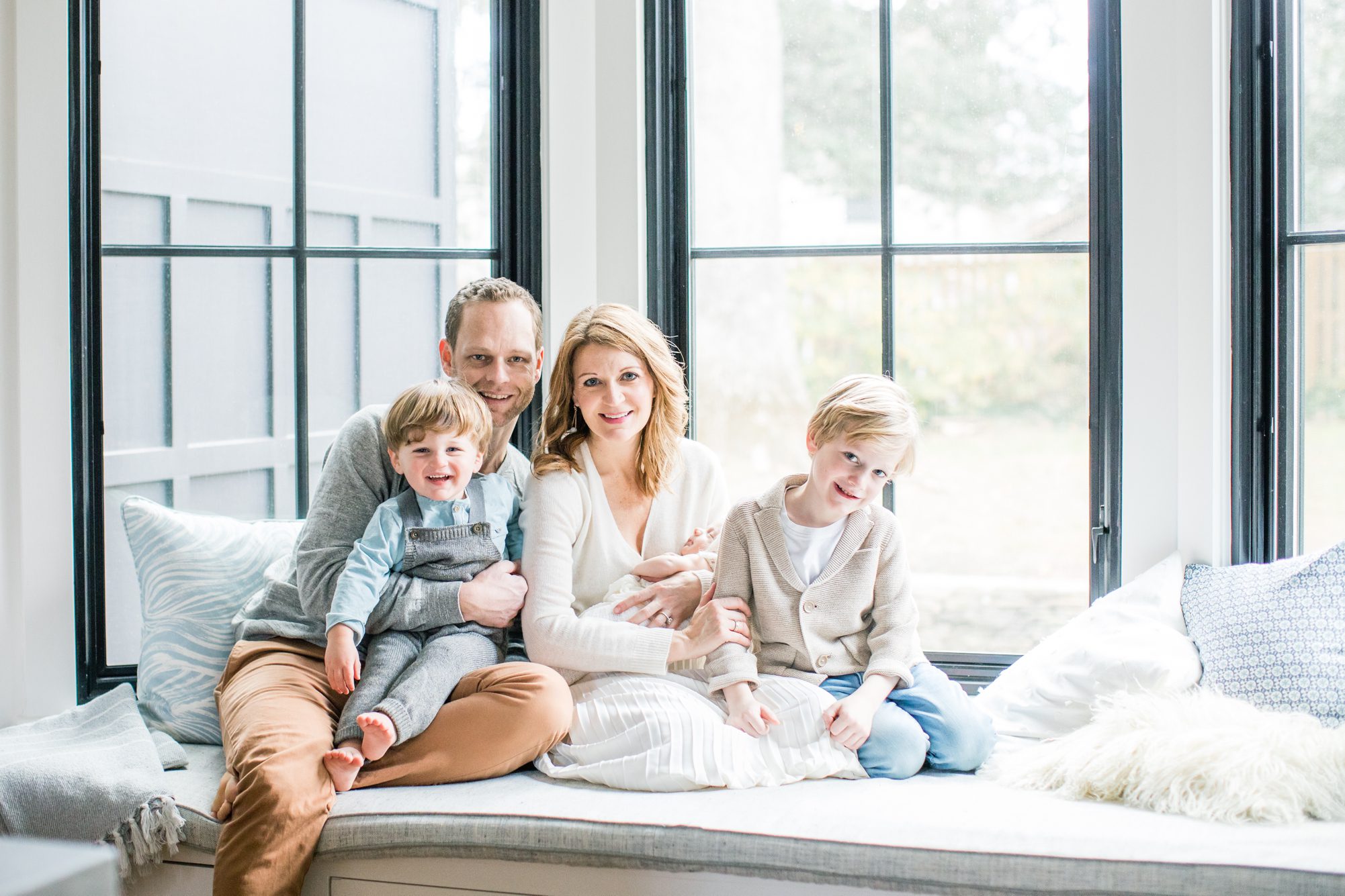 Parents with three boys on window seat during in-home newborn session. Photo by Chevy Chase DC Newborn photographer, LRG Portraits.