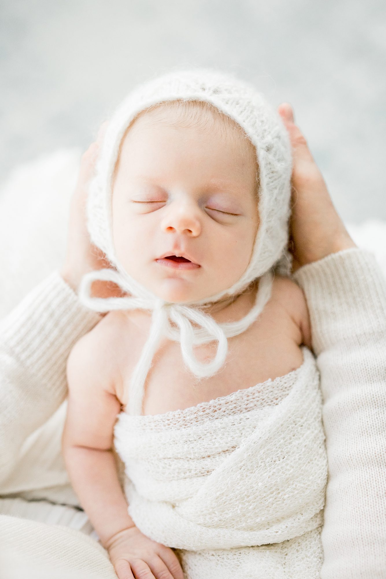 Closeup of baby wearing white bonnet in Chevy Chase, DC newborn session. Photo by LRG Portraits