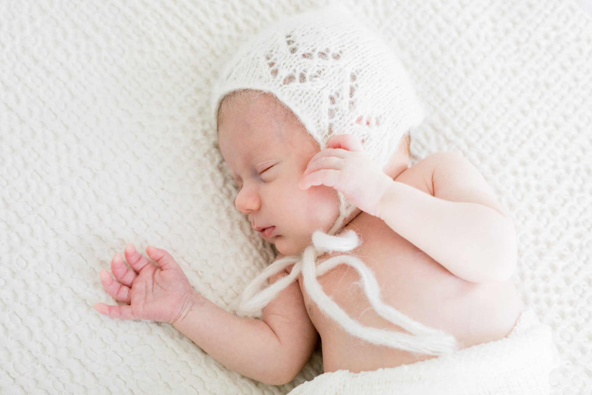 Baby in white bonnet and swaddle during newborn session. Photo by LRG Portraits