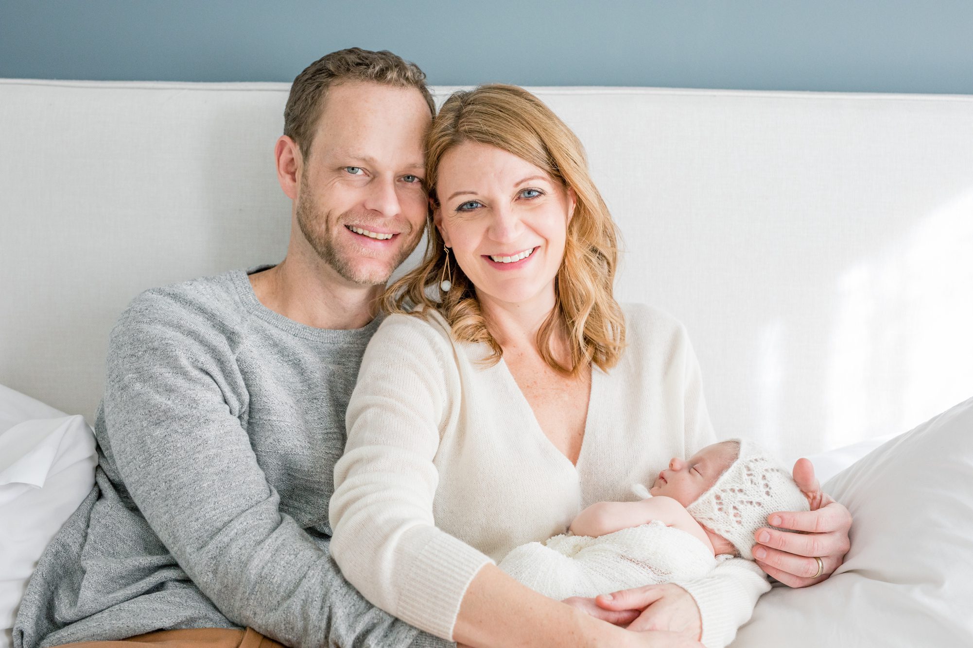 Mom and Dad holding baby on bed during newborn session. Photo by LRG Portraits