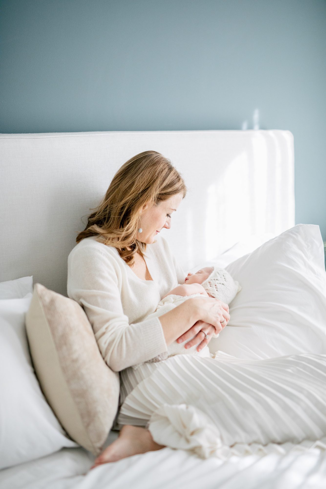 Mom relaxing on bed holding baby during newborn session. Photo by Chevy Chase DC newborn photographer, LRG Portraits.