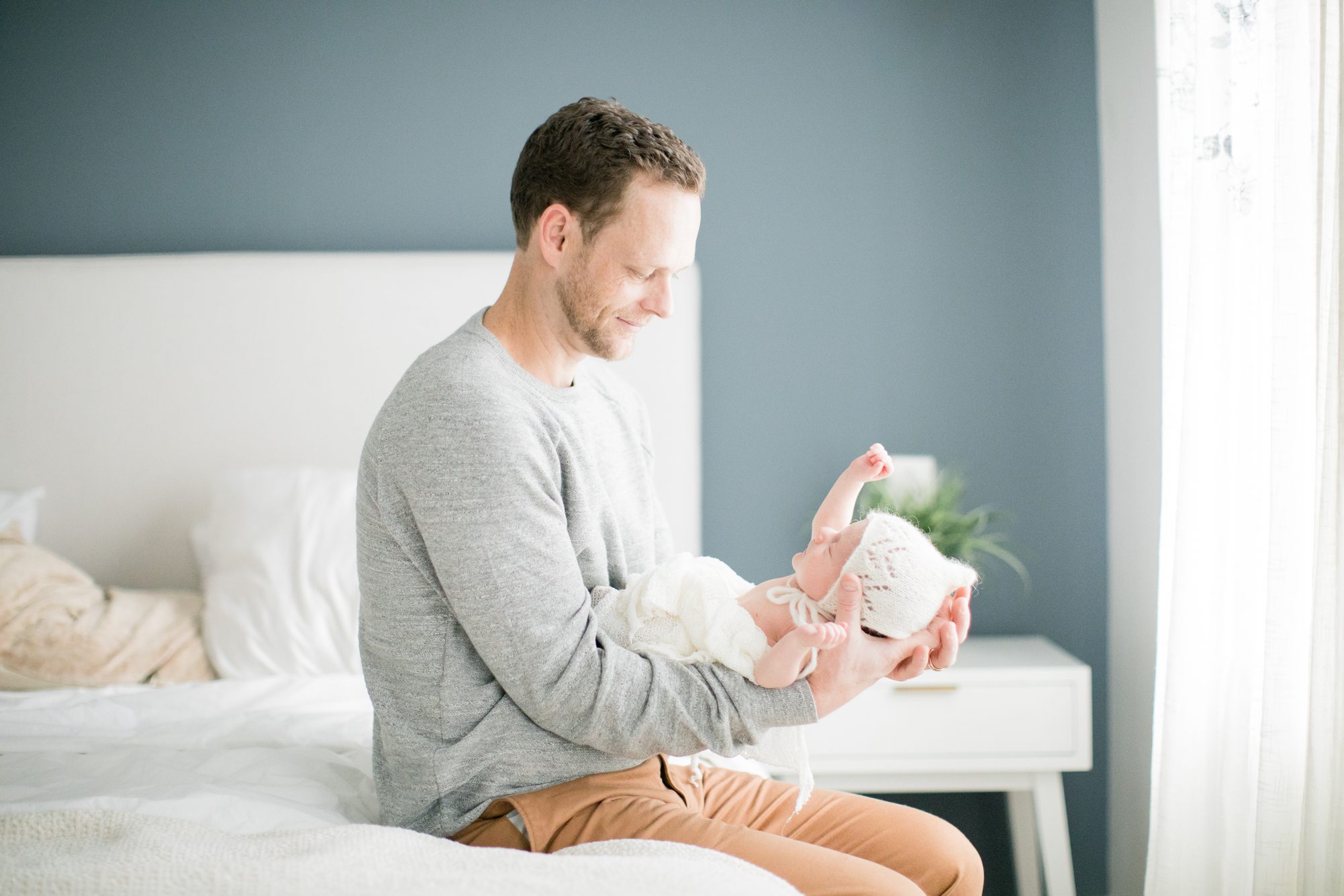 Dad holding baby on bed while baby stretches. Photo by LRG Portraits