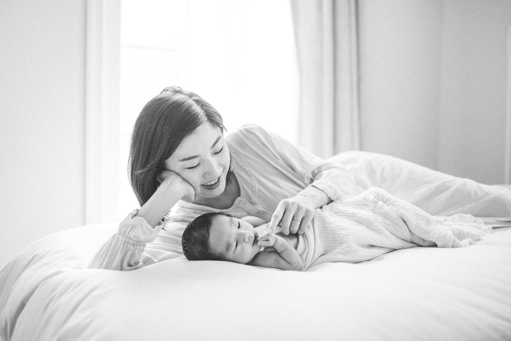Black and white image of Mom laying on bed next to baby by Bethesda, MD lifestyle newborn photographer, LRG Portraits.