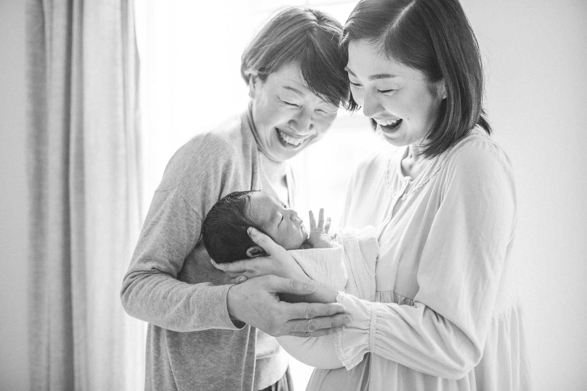 Joyful black and white image of Mom with baby and Grandma during in-home newborn session. Photo by LRG Portraits.
