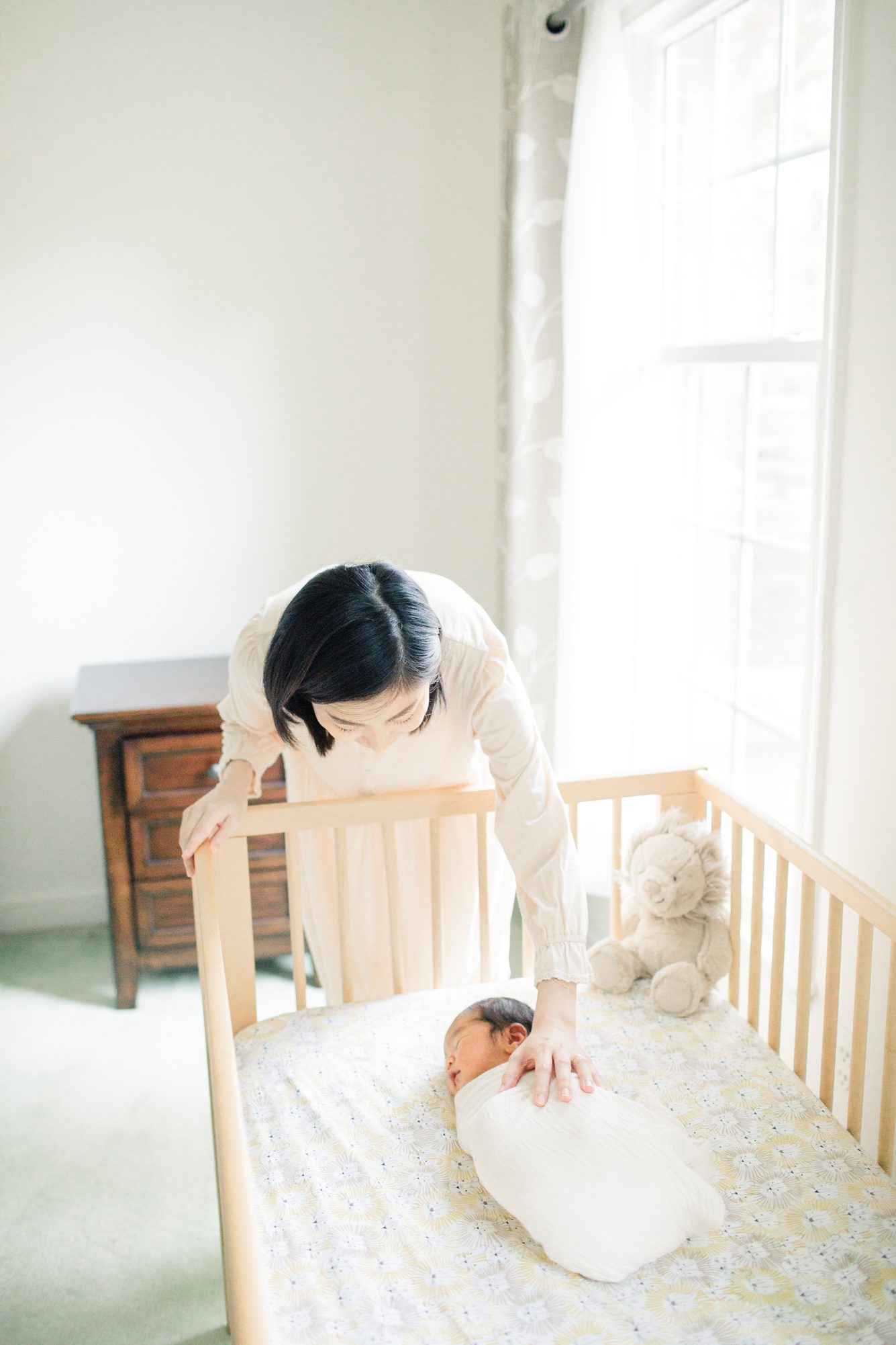 Mom reaching into crib to soothe baby during newborn photo shoot in Bethesda, MD. Photo by LRG Portraits.
