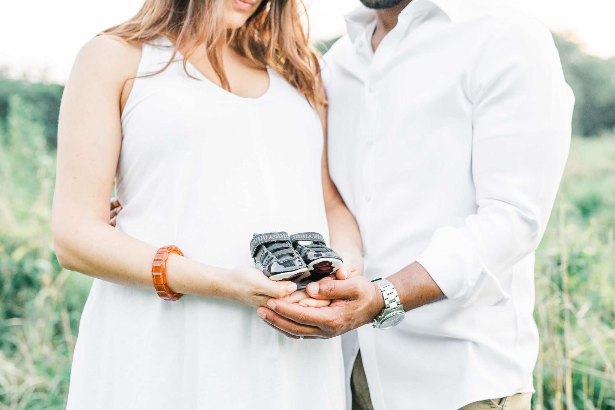 Parents holding infant shoes during field maternity session. Photo by Washington DC photographer, LRG Portraits