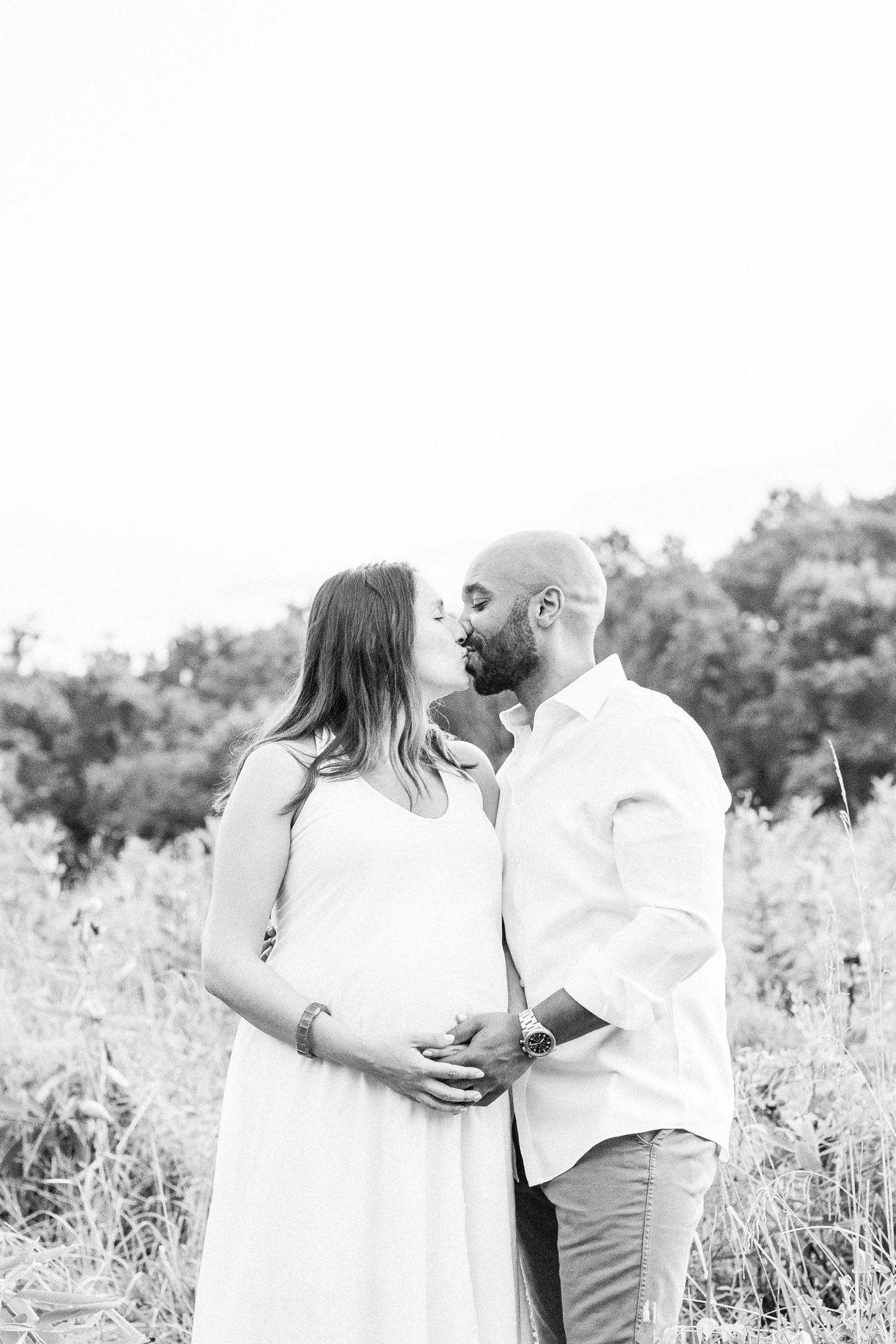Black and white image of parents kissing during maternity session. Photo by LRG Portraits