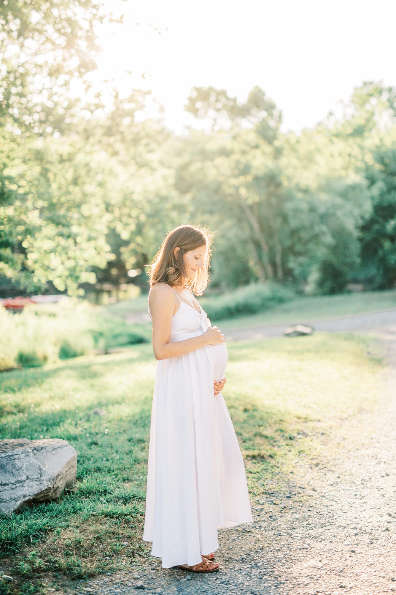 Beautiful film-inspired image of mom hugging baby bump on path near the Potomac River. Photo by LRG Portraits.