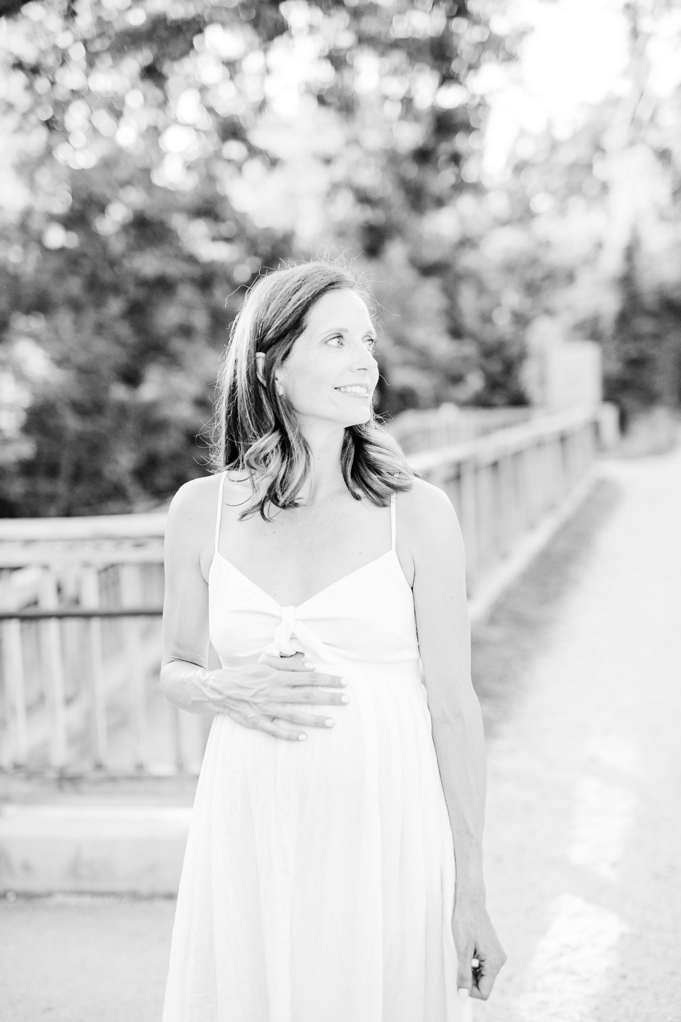 Black and white image of expecting mom looking away with one hand on belly. Photo by LRG Portraits.