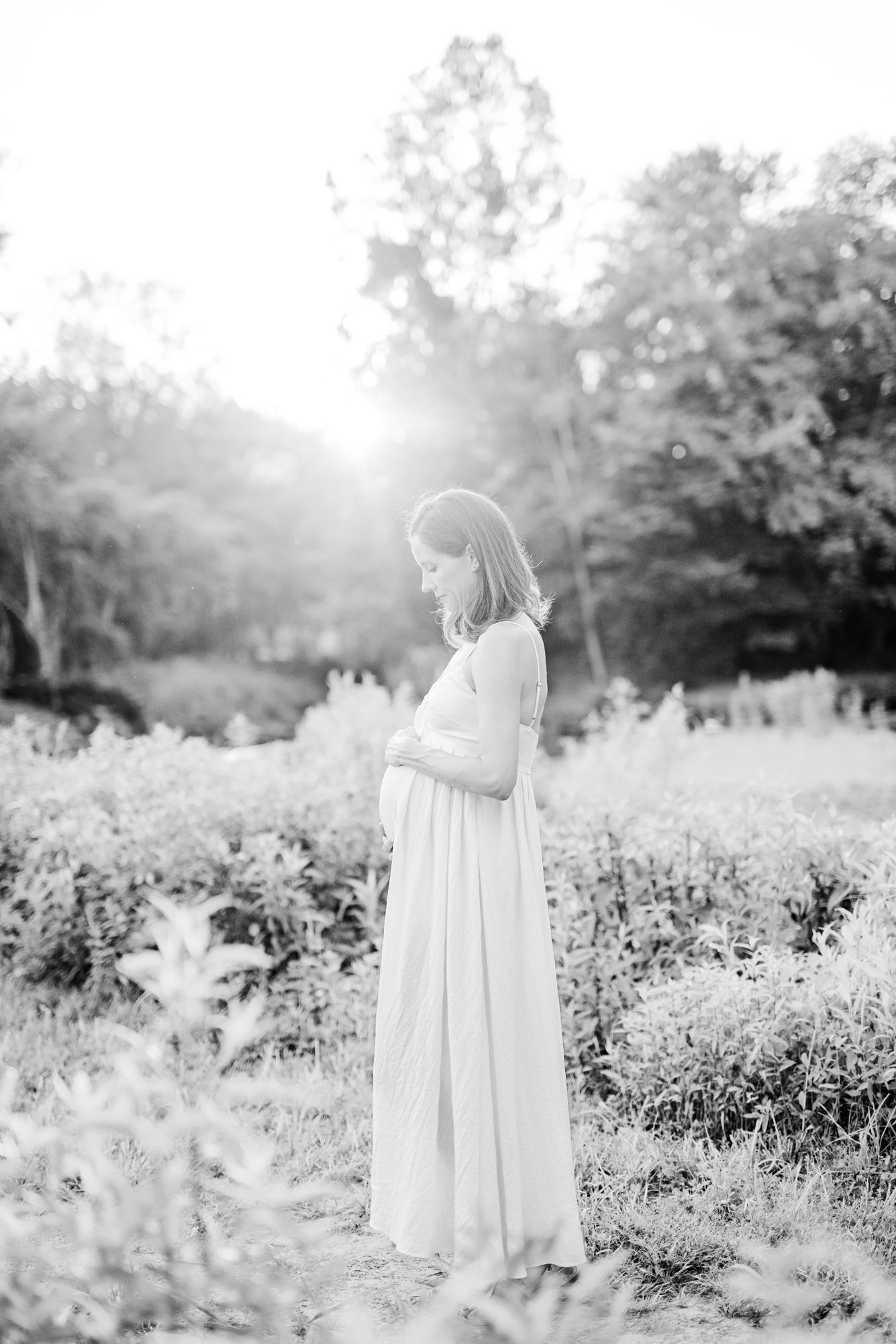 Black and white image of Mom with baby bump with beautiful sunlight shining behind her. Photo by LRG Portraits.