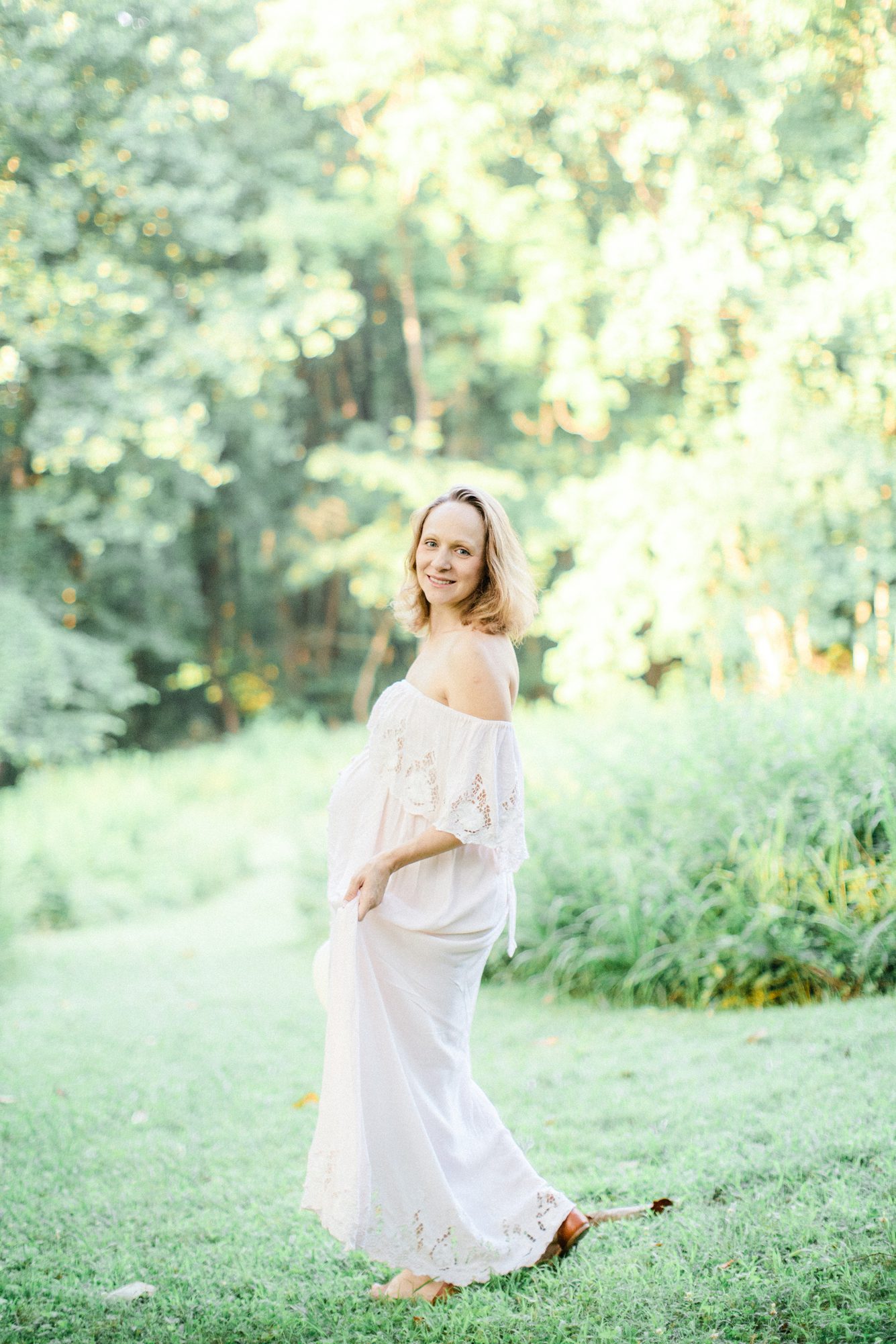 Mom walking in field holding dress during maternity session. Photo by LRG Portraits.