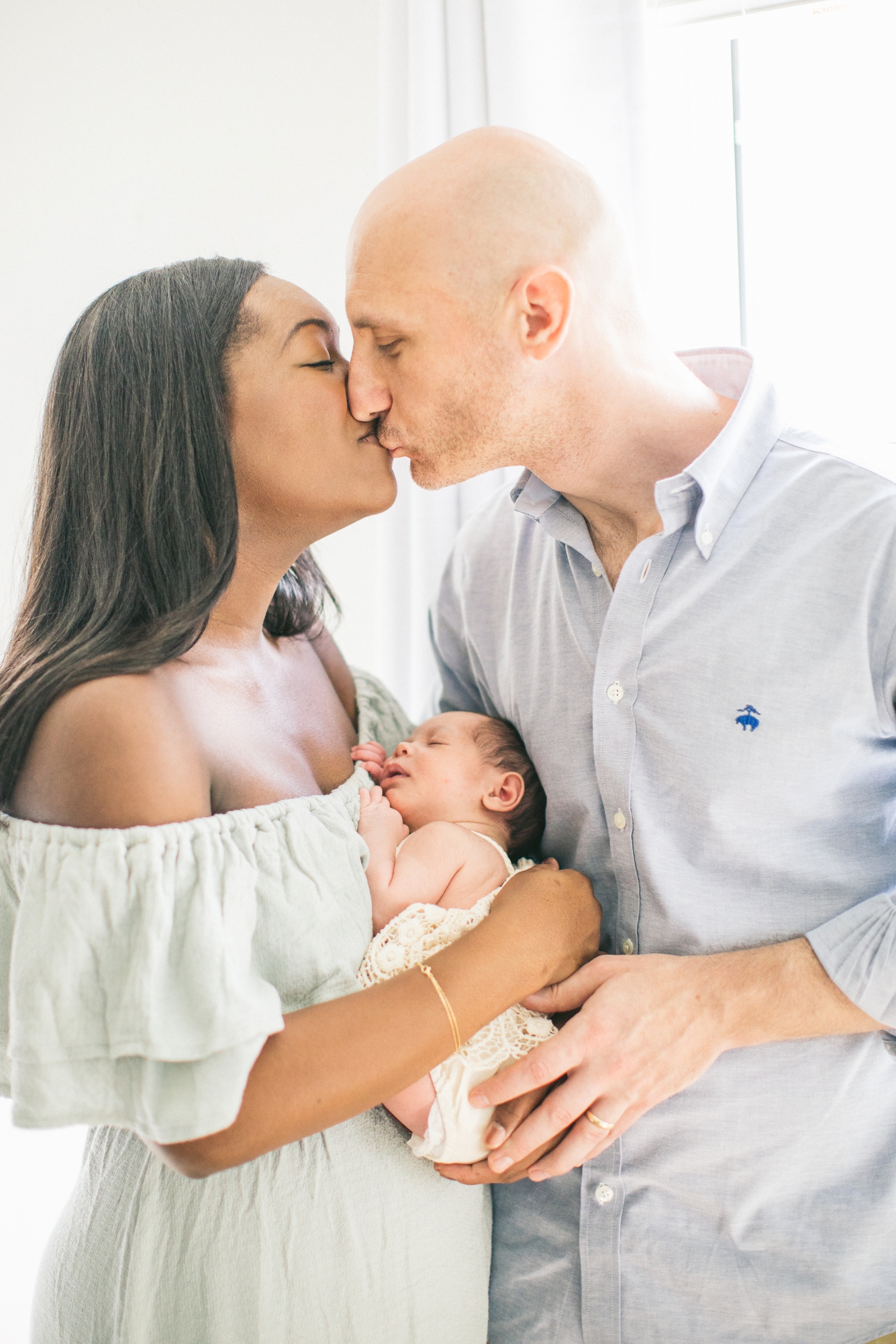Mom and Dad kiss while holding baby during newborn session. Photo by LRG Portraits.