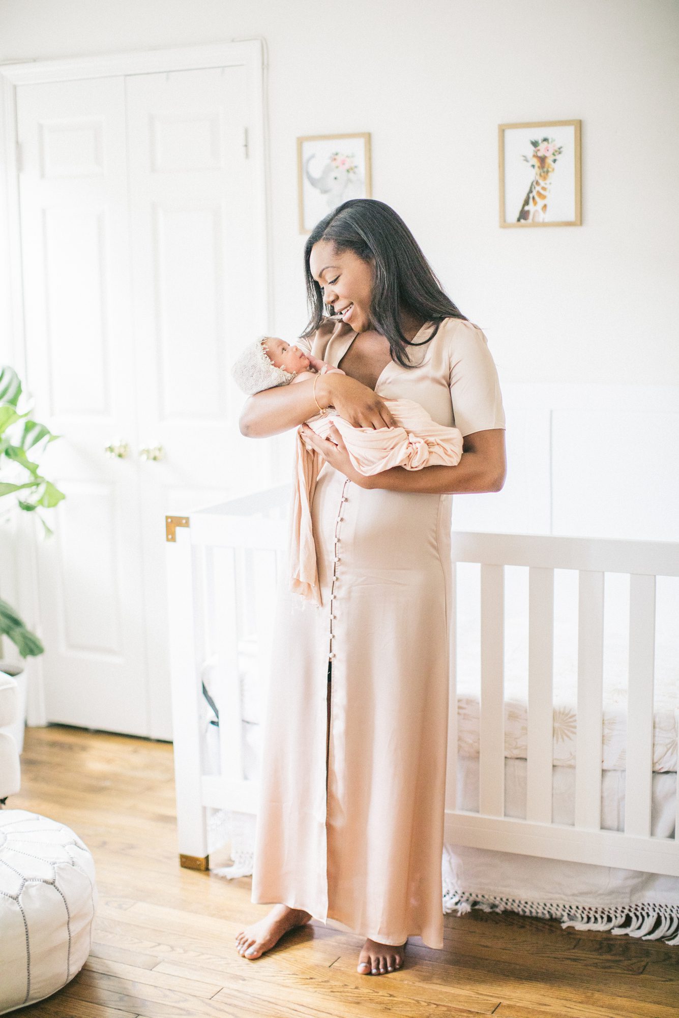 Mom wearing blush maxi dress looking down at baby in her arms during lifestyle newborn session in Washington DC.Photo by LRG Portraits.