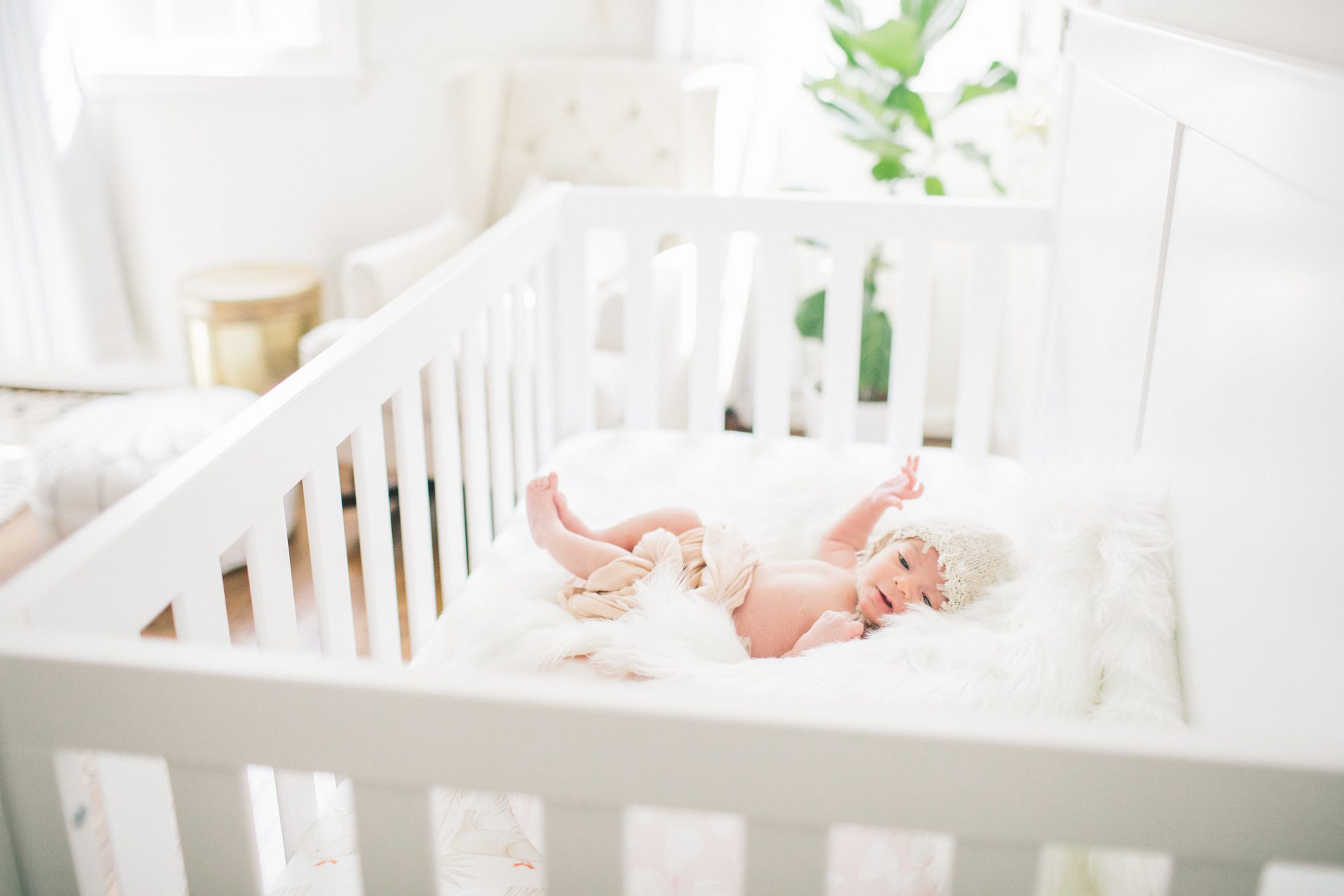 Newborn baby girl in crib wearing bonnet. Photo by LRG Portraits.
