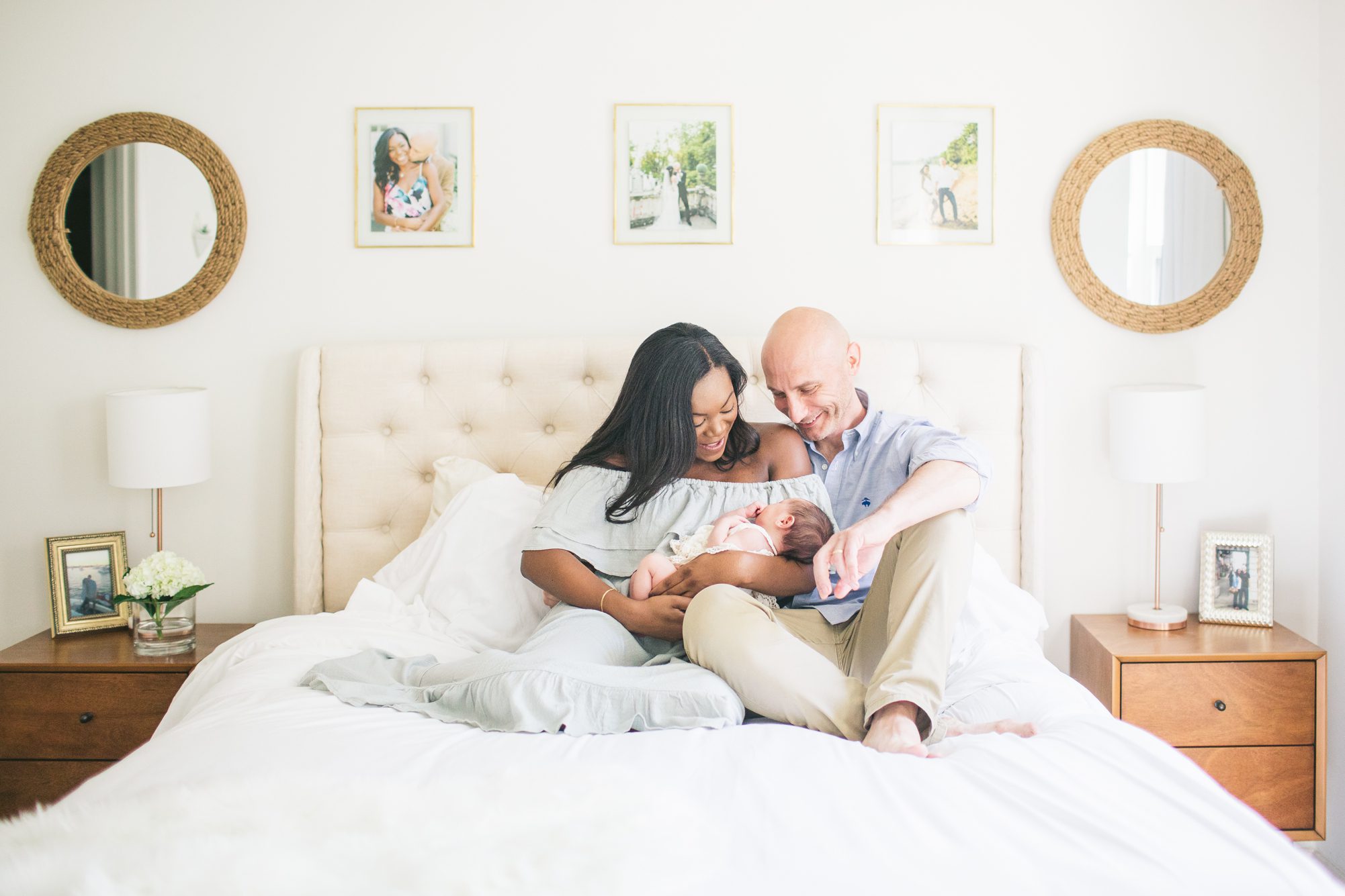 Mom and Dad on bed holding baby girl during Washington DC lifestyle newborn session. Photo by LRG Portraits.