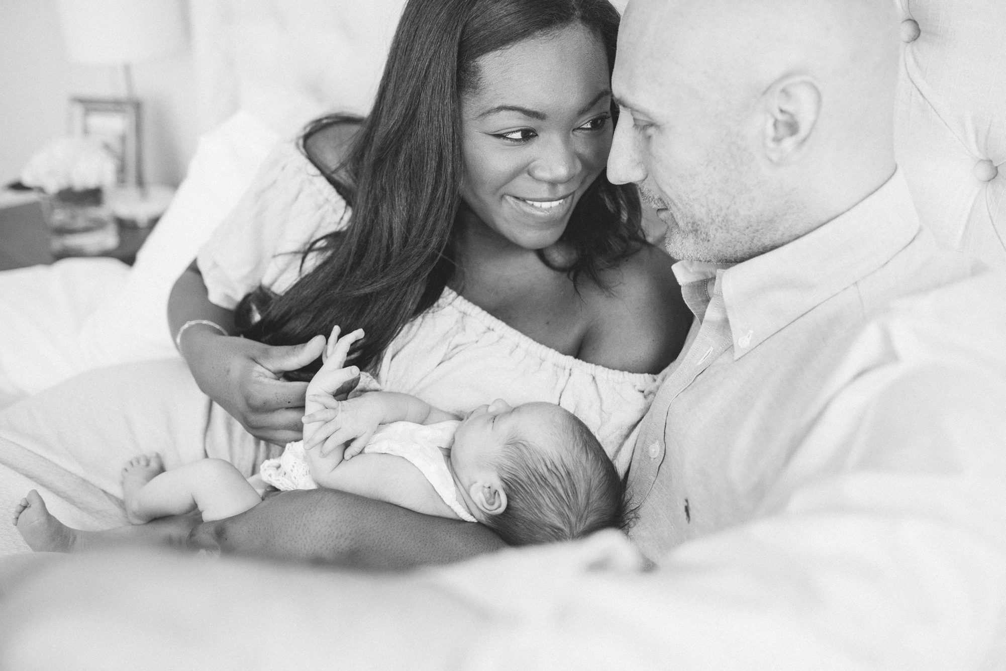 Black and white image of parents holding baby on bed during newborn session. Photo by LRG Portraits.