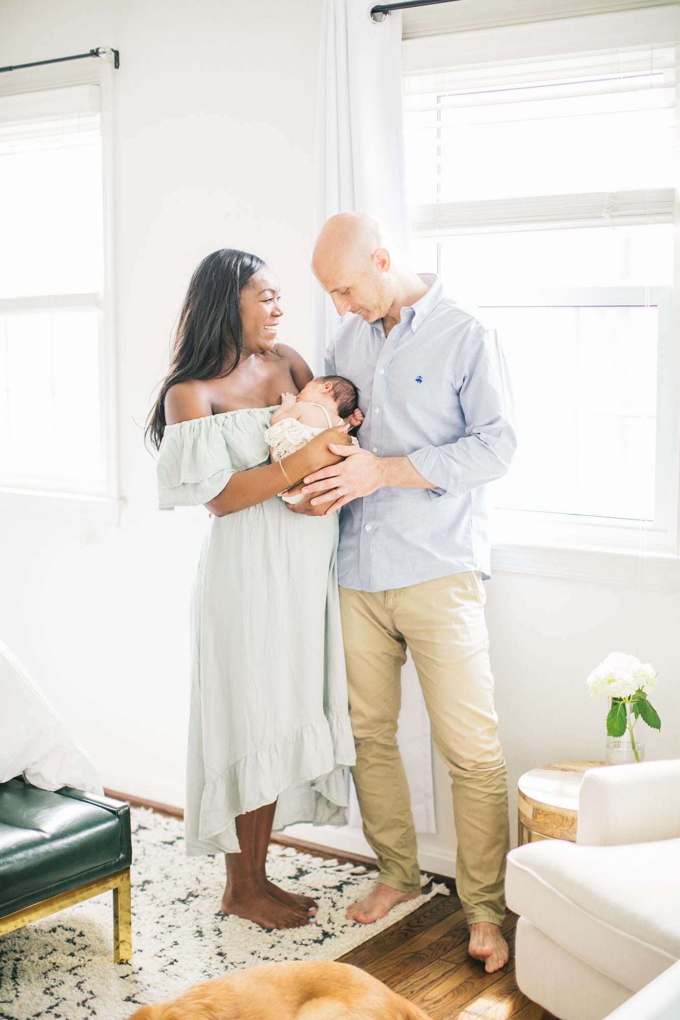 New parents holding baby and smiling near windows of bedroom. Photo by LRG Portraits.