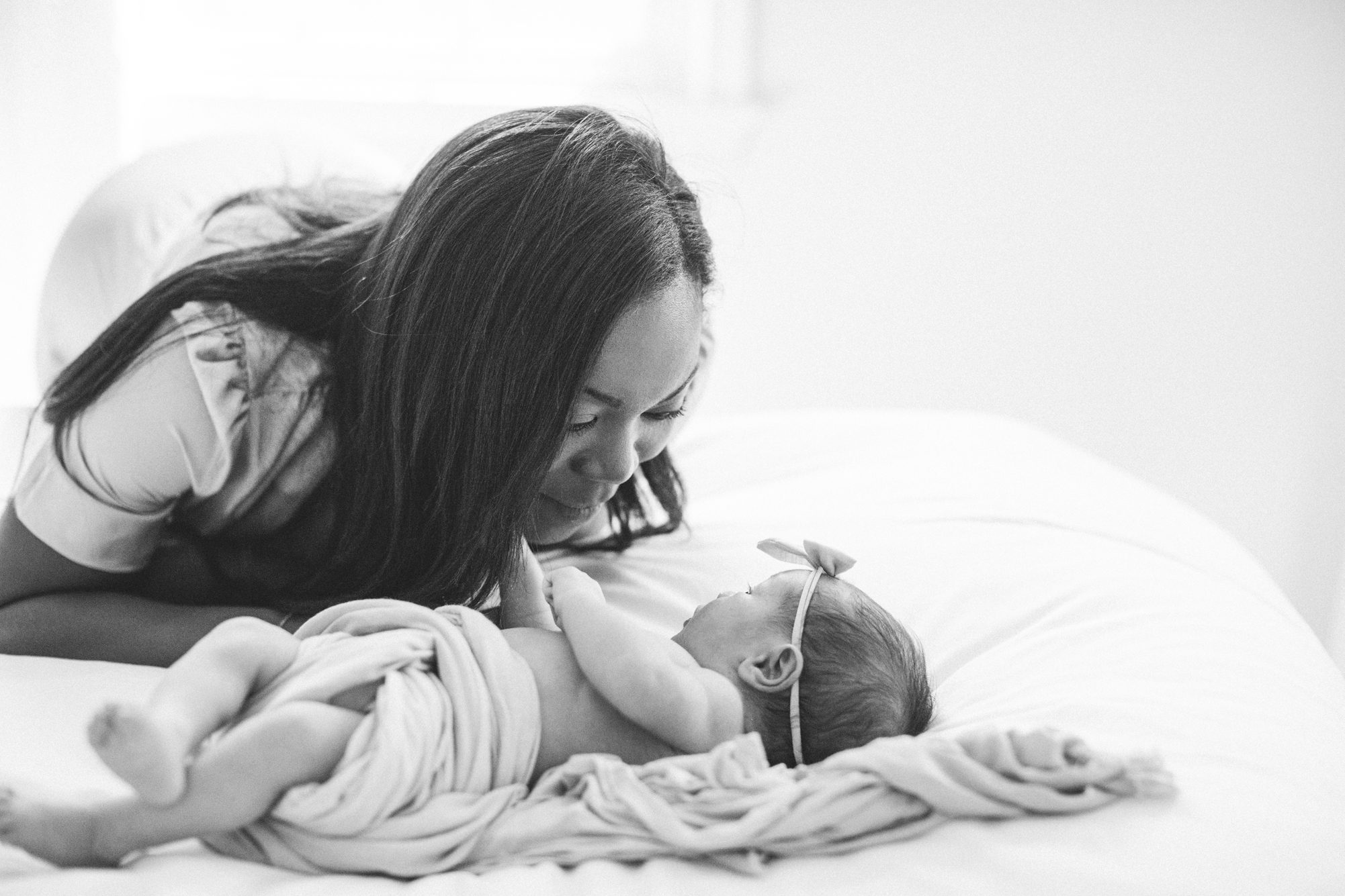 Black and white image of Mom talking to baby girl on bed during lifestyle newborn session in Washington DC. Photo by LRG Portraits.