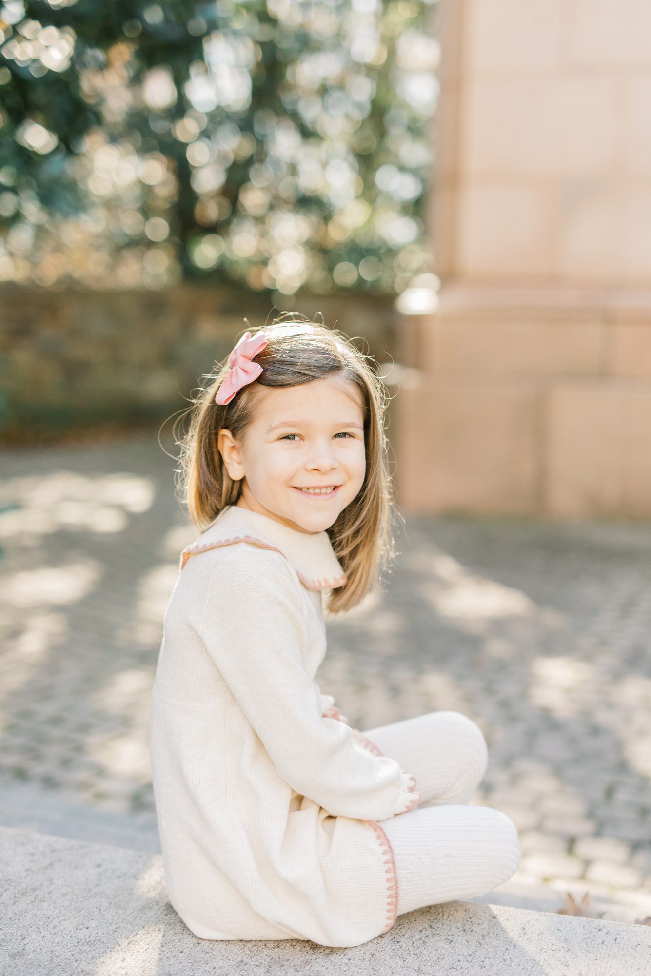 Little girl smiling at photo while wearing white sweater dress. Photo by Washington DC family photographer, LRG Portraits.